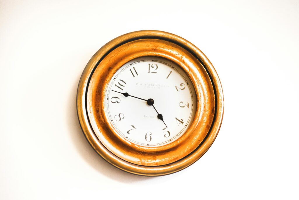A stylish vintage wall clock with a golden frame and white face photographed against a bright white background.